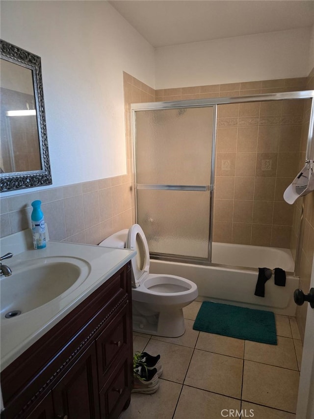 full bathroom featuring tile patterned floors, toilet, shower / bath combination with glass door, vanity, and tile walls