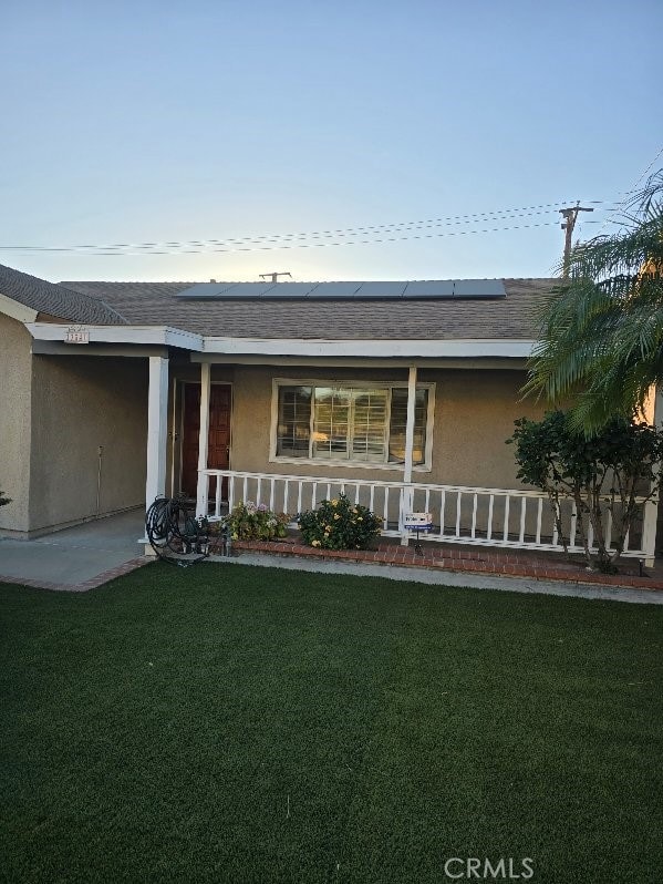 ranch-style house with solar panels, a porch, and a front yard