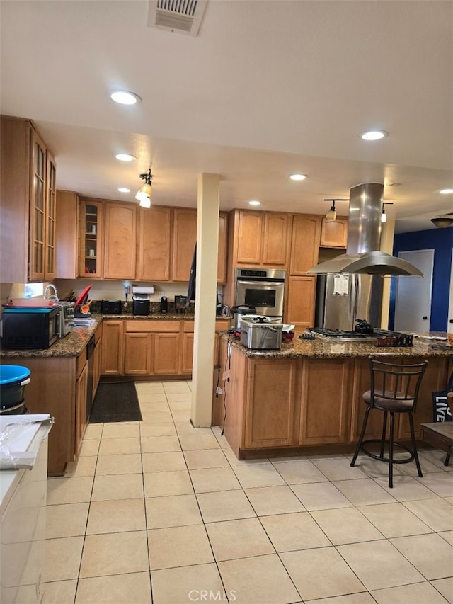 kitchen featuring dark stone countertops, island range hood, oven, and light tile patterned floors