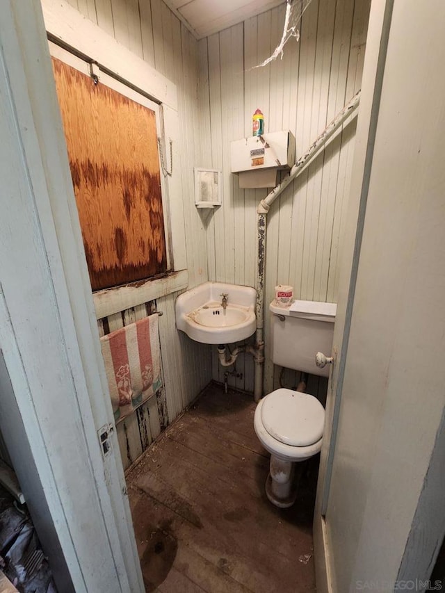 bathroom with toilet, wood walls, sink, and hardwood / wood-style floors