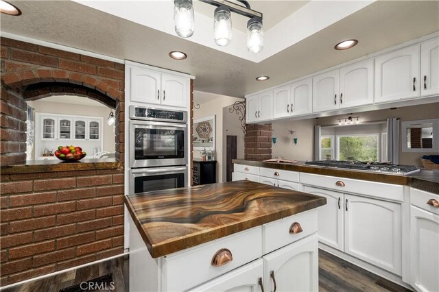 kitchen with hanging light fixtures, brick wall, dark wood-type flooring, appliances with stainless steel finishes, and white cabinets