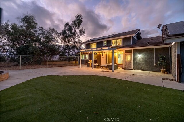 back house at dusk featuring an outdoor living space, a patio area, and a lawn