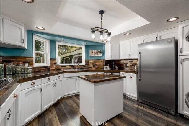 kitchen with hanging light fixtures, a raised ceiling, stainless steel refrigerator, a center island, and white cabinetry