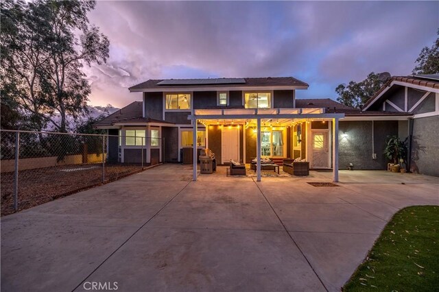 back house at dusk with a pergola, an outdoor hangout area, solar panels, and a patio area