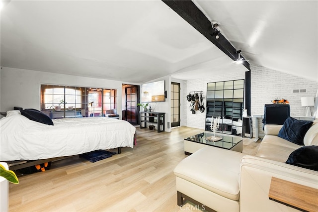 bedroom with lofted ceiling with beams, track lighting, brick wall, and light wood-type flooring