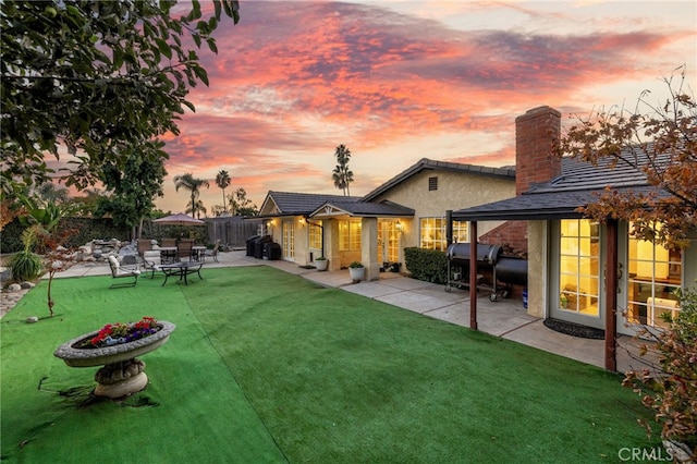 back house at dusk featuring a patio and a lawn