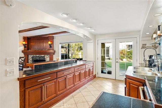 kitchen with french doors, beam ceiling, sink, light tile patterned flooring, and a fireplace