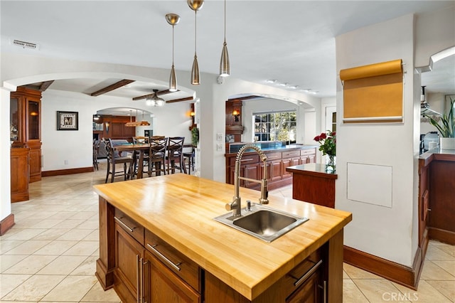 kitchen with an island with sink, wood counters, sink, decorative light fixtures, and light tile patterned floors