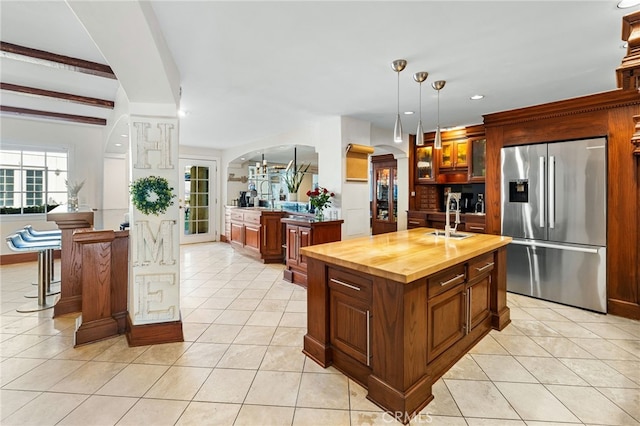 kitchen with sink, wood counters, hanging light fixtures, stainless steel fridge with ice dispenser, and a kitchen island with sink