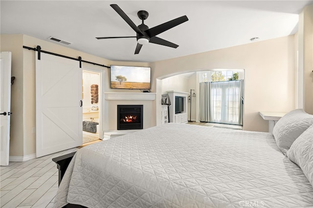 bedroom featuring a barn door, connected bathroom, and ceiling fan