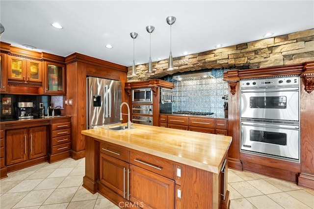 kitchen with hanging light fixtures, a center island with sink, appliances with stainless steel finishes, sink, and butcher block countertops