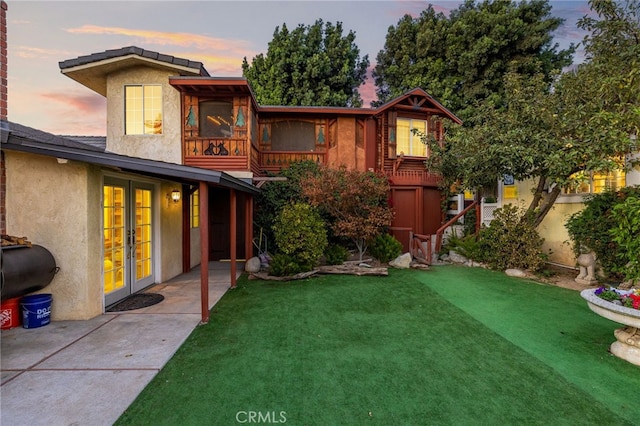 back house at dusk featuring a yard and a patio