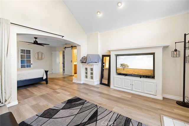 interior space with ceiling fan, high vaulted ceiling, light wood-type flooring, and a barn door