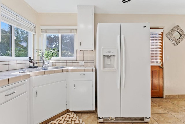 kitchen with tile counters, white cabinetry, white refrigerator with ice dispenser, tasteful backsplash, and sink