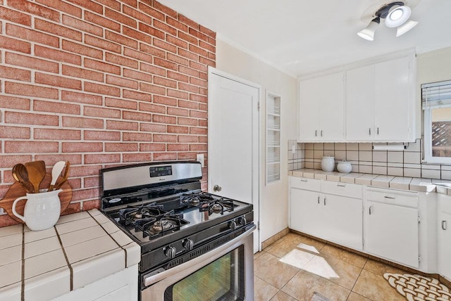 kitchen featuring backsplash, gas stove, light tile patterned flooring, tile counters, and white cabinets