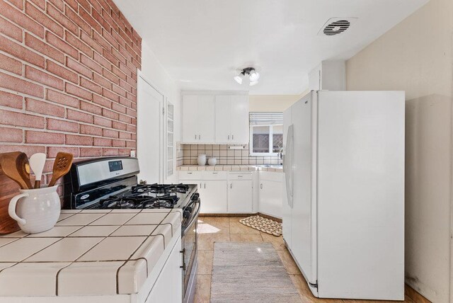 kitchen featuring tile countertops, gas stove, white fridge, light tile patterned floors, and white cabinets