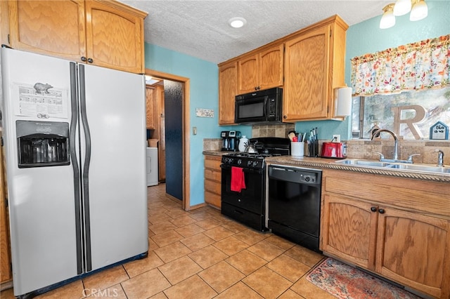 kitchen featuring a textured ceiling, sink, black appliances, light tile patterned floors, and washer / clothes dryer