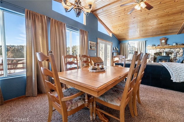 carpeted dining room with lofted ceiling, french doors, ceiling fan with notable chandelier, a stone fireplace, and wood ceiling