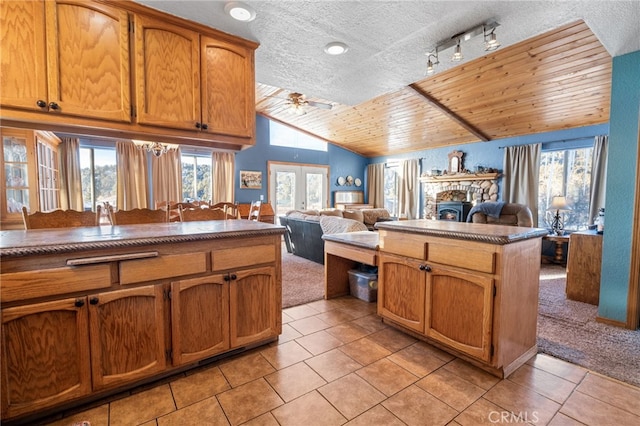 kitchen featuring light carpet, a textured ceiling, ceiling fan with notable chandelier, vaulted ceiling, and a fireplace