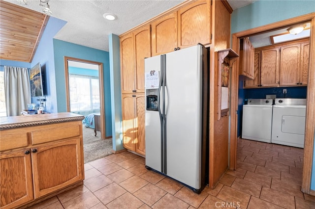 kitchen with refrigerator with ice dispenser, light tile patterned floors, a textured ceiling, and washer and clothes dryer