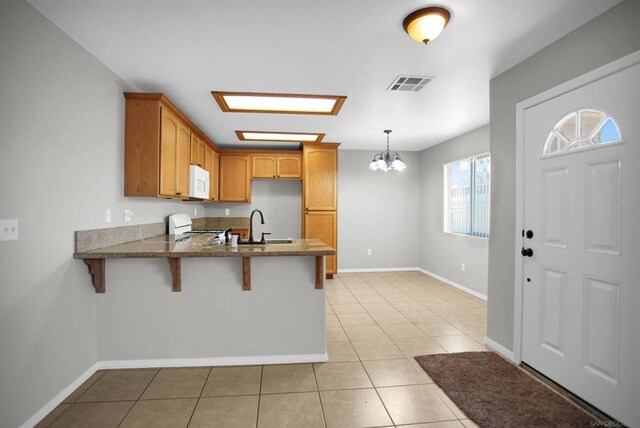 kitchen with stove, sink, light tile patterned floors, decorative light fixtures, and a breakfast bar area