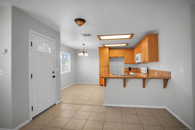 kitchen with kitchen peninsula, a breakfast bar, white appliances, pendant lighting, and light tile patterned flooring