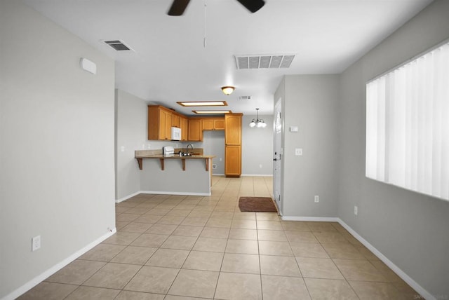 kitchen with a kitchen breakfast bar, kitchen peninsula, decorative light fixtures, light tile patterned floors, and ceiling fan with notable chandelier