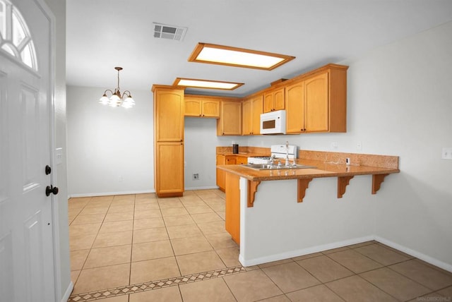 kitchen featuring a kitchen bar, white appliances, kitchen peninsula, and light tile patterned flooring