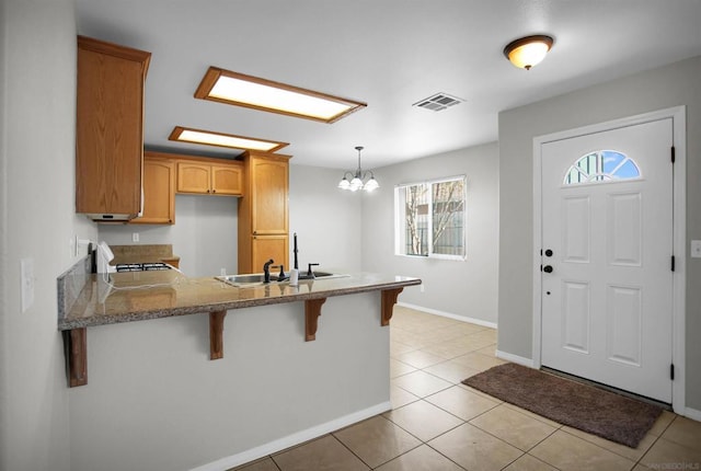 kitchen with a notable chandelier, kitchen peninsula, light tile patterned floors, and sink