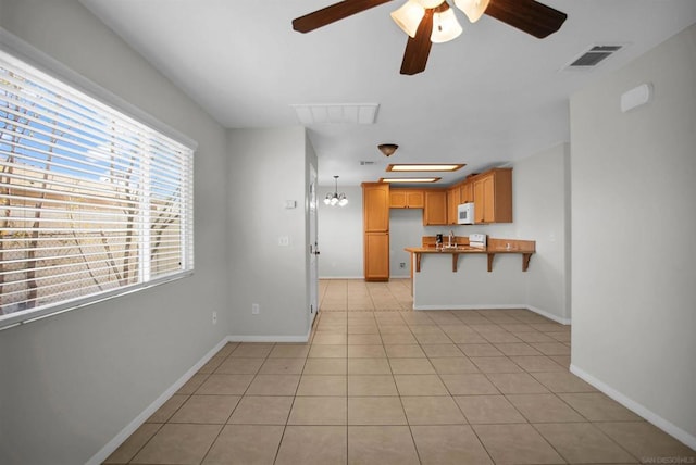 kitchen with kitchen peninsula, light tile patterned floors, ceiling fan, and sink