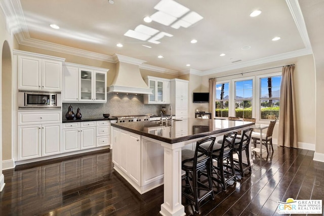 kitchen with stainless steel microwave, a large island with sink, white cabinets, and premium range hood