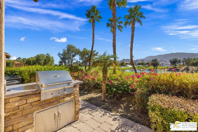 view of patio with a grill, a water and mountain view, and an outdoor kitchen