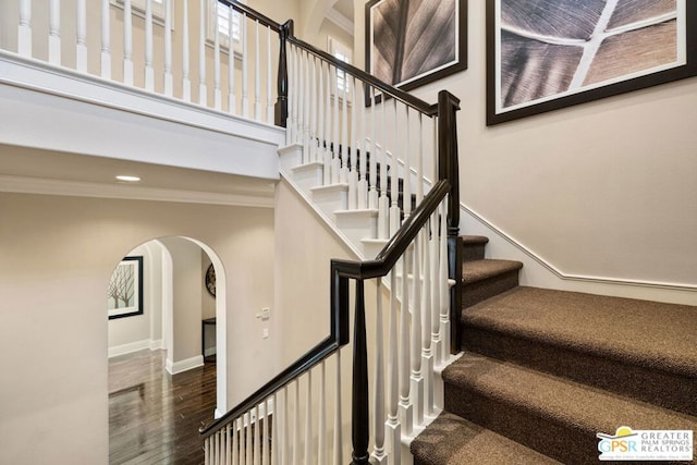 staircase with hardwood / wood-style flooring, a towering ceiling, and crown molding