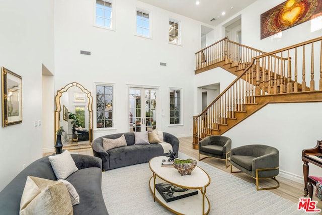 living room featuring a high ceiling, light hardwood / wood-style flooring, french doors, and a healthy amount of sunlight