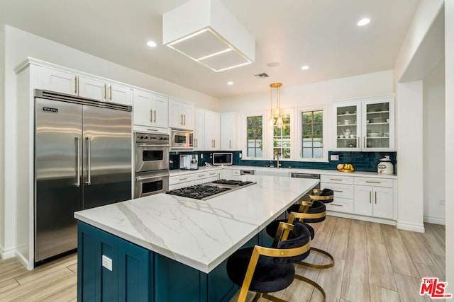 kitchen with pendant lighting, light hardwood / wood-style flooring, built in appliances, tasteful backsplash, and a kitchen island