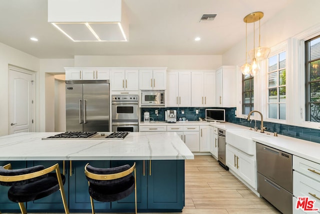 kitchen featuring white cabinetry, sink, built in appliances, decorative light fixtures, and a kitchen island