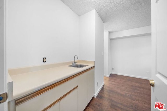 bar featuring a textured ceiling, dark hardwood / wood-style flooring, white cabinetry, and sink