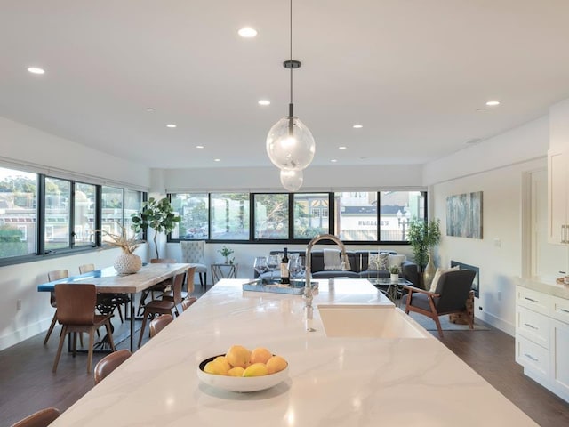 kitchen with white cabinetry, light stone countertops, hanging light fixtures, and a wealth of natural light