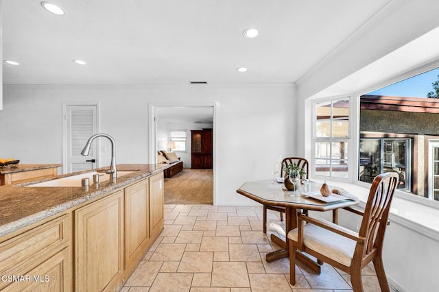 kitchen with light brown cabinets, light stone counters, a healthy amount of sunlight, and sink