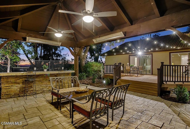 patio terrace at dusk featuring a gazebo, ceiling fan, a deck, and an outdoor bar