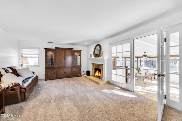 carpeted living room featuring a fireplace, french doors, ceiling fan, and crown molding