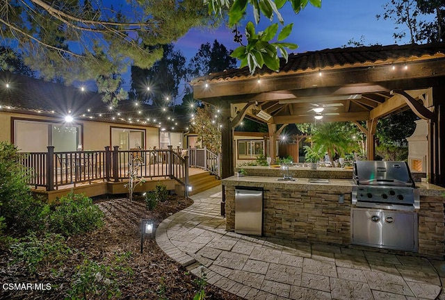 patio terrace at dusk with a gazebo, area for grilling, grilling area, and a wooden deck