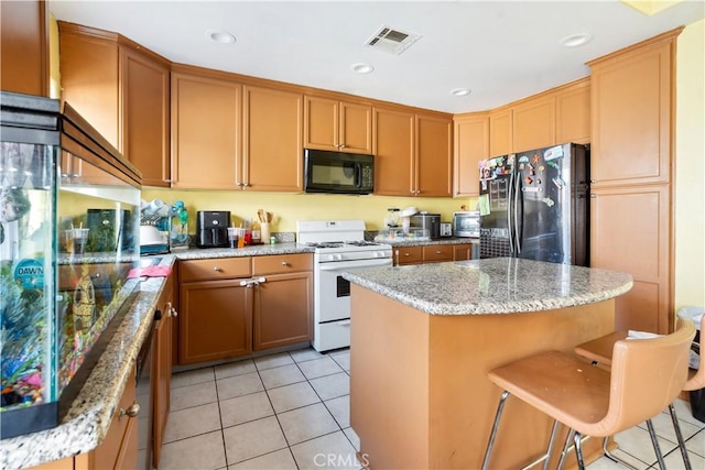 kitchen with black appliances, a kitchen breakfast bar, a center island, and light stone counters