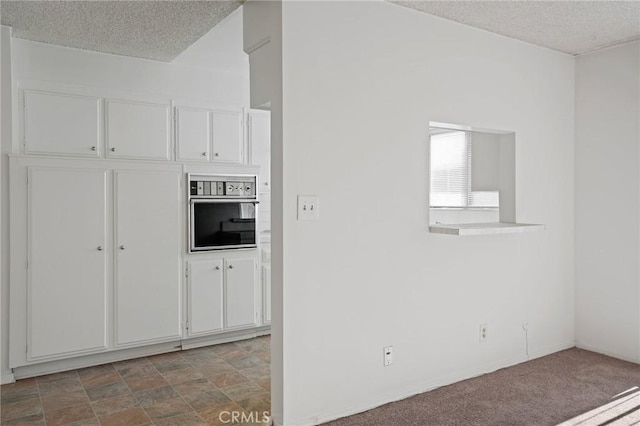 kitchen with white cabinets, stainless steel oven, a textured ceiling, and carpet