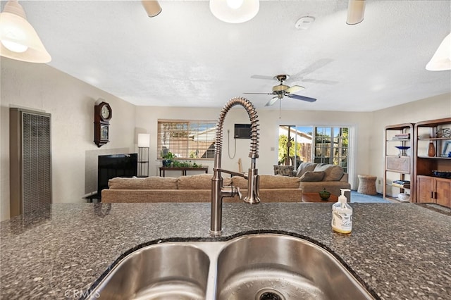 kitchen with a textured ceiling, sink, and dark stone counters