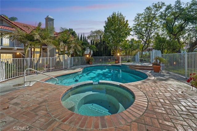 pool at dusk with a patio area and an in ground hot tub