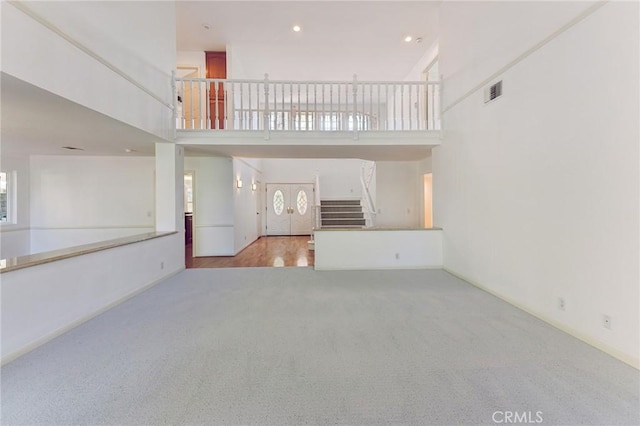 unfurnished living room featuring light carpet and a towering ceiling