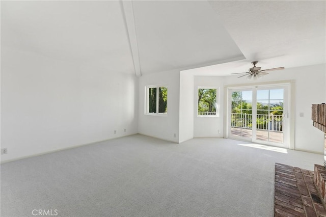 unfurnished living room featuring vaulted ceiling with beams, ceiling fan, light colored carpet, and a wealth of natural light