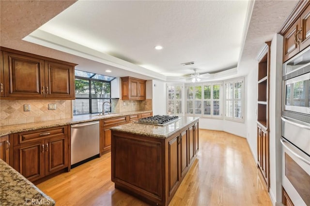 kitchen with a raised ceiling, light hardwood / wood-style flooring, a kitchen island, and stainless steel appliances