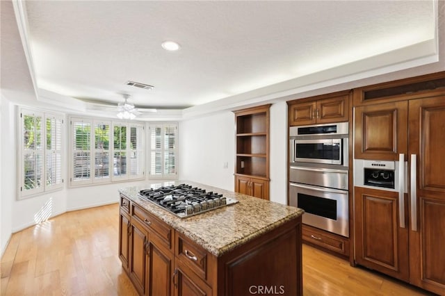 kitchen with ceiling fan, light stone counters, light wood-type flooring, a kitchen island, and appliances with stainless steel finishes